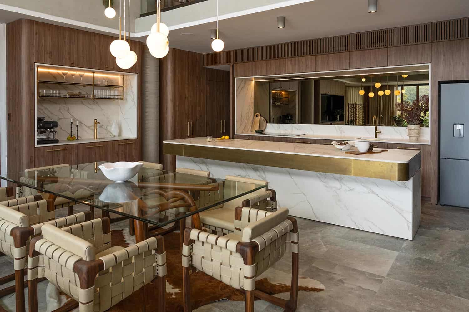 Modern kitchen with marble island, wood cabinetry, and a glass dining table with woven chairs