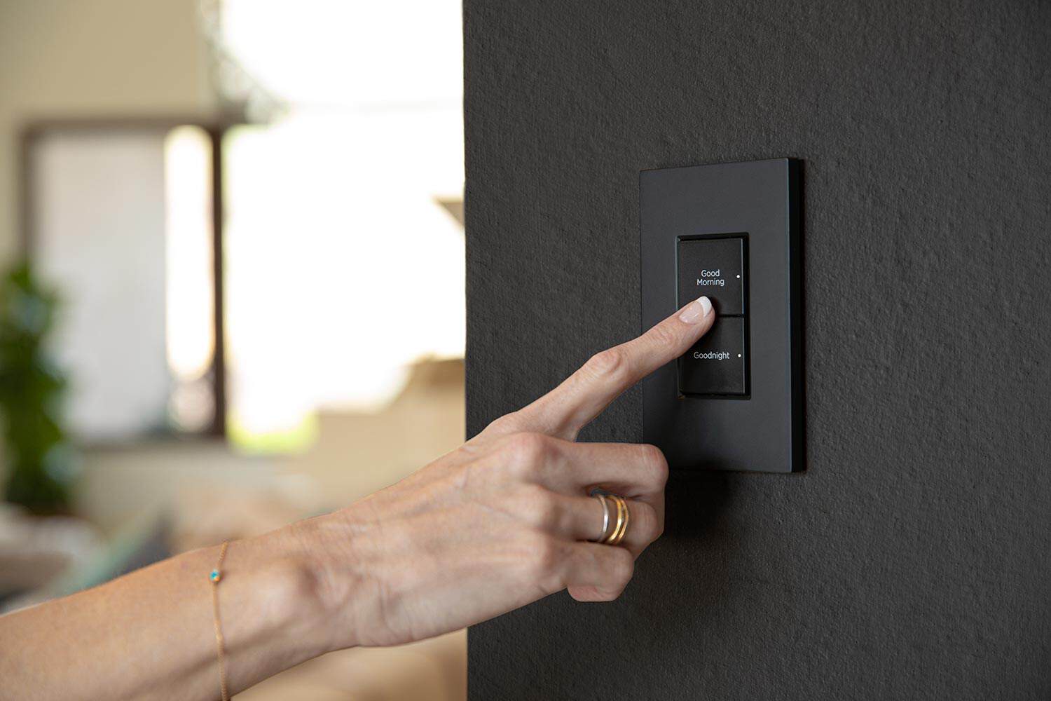 Person pressing a black wall-mounted keypad labeled Good Morning and Goodnight