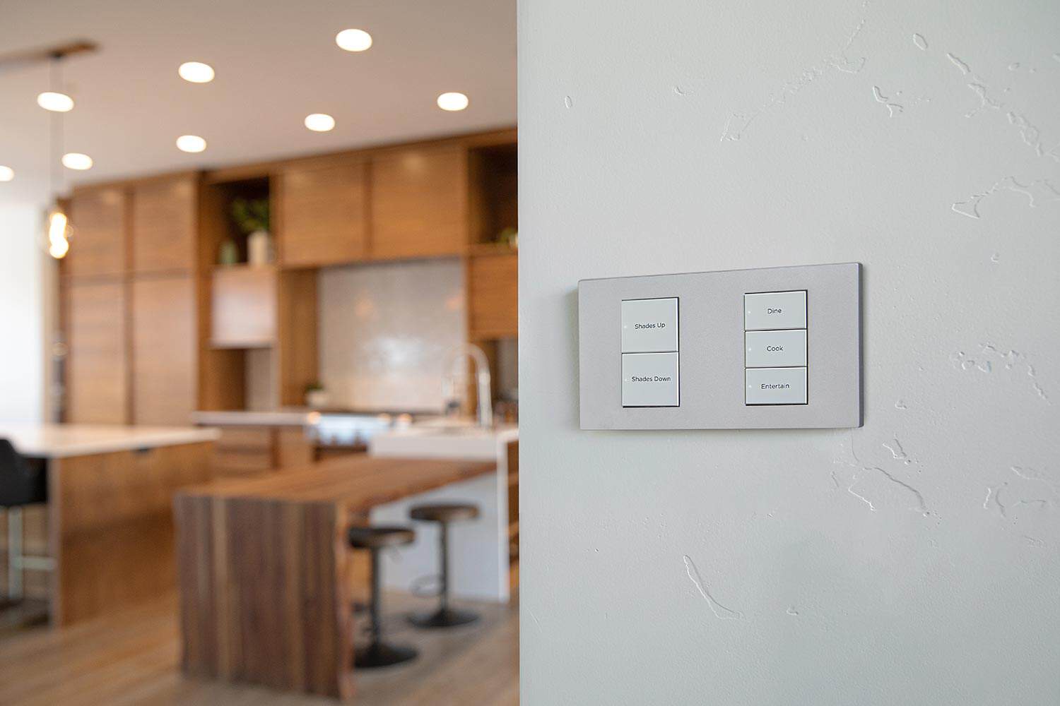 Silver wall-mounted smart lighting keypad with labeled buttons in a modern home