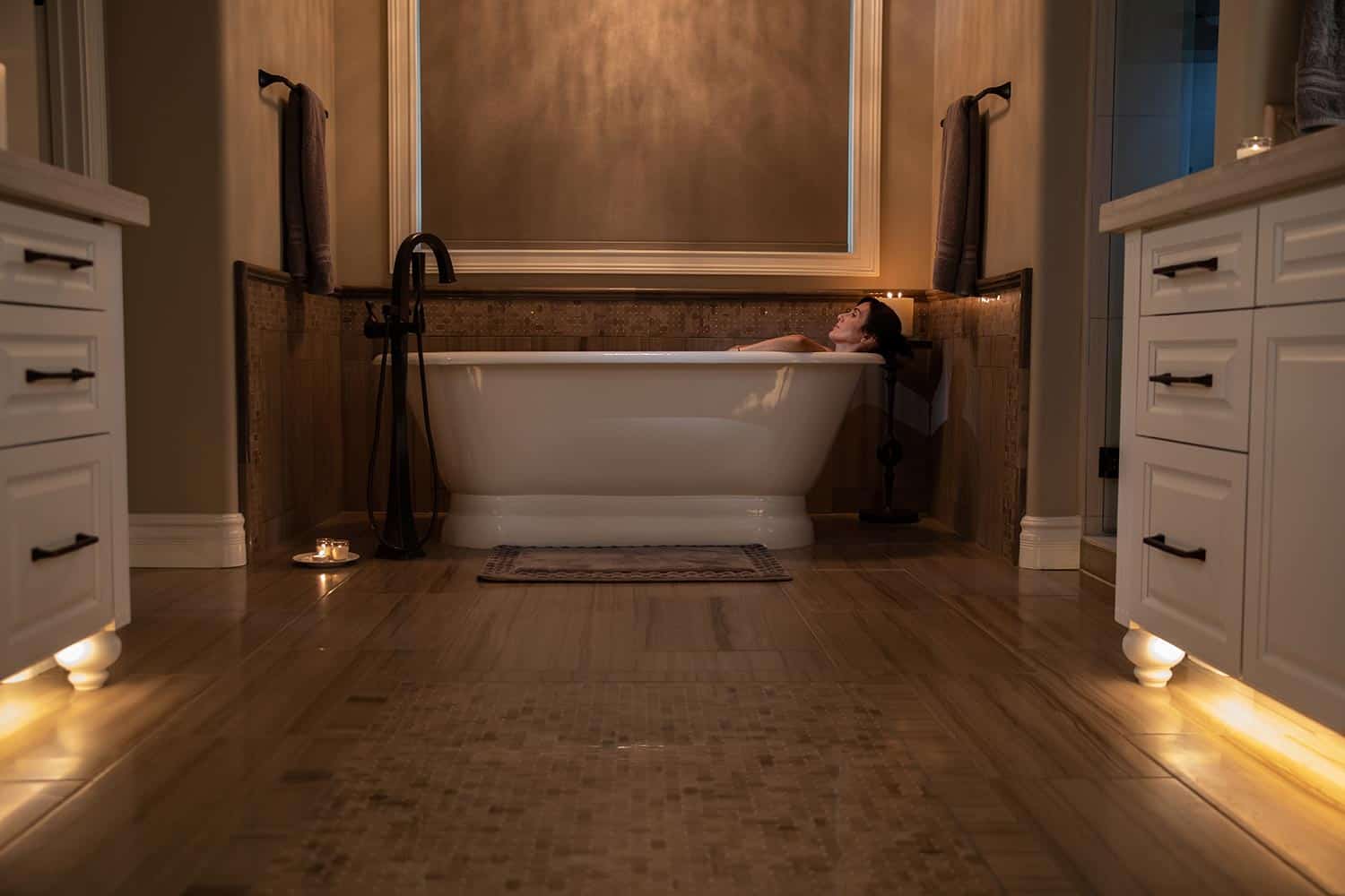 Woman relaxing in a white pedestal bathtub with warm under-cabinet lighting