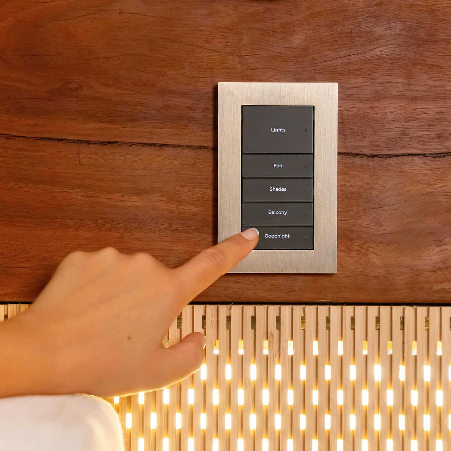 Finger pressing the goodnight button on a sleek metal wall keypad
