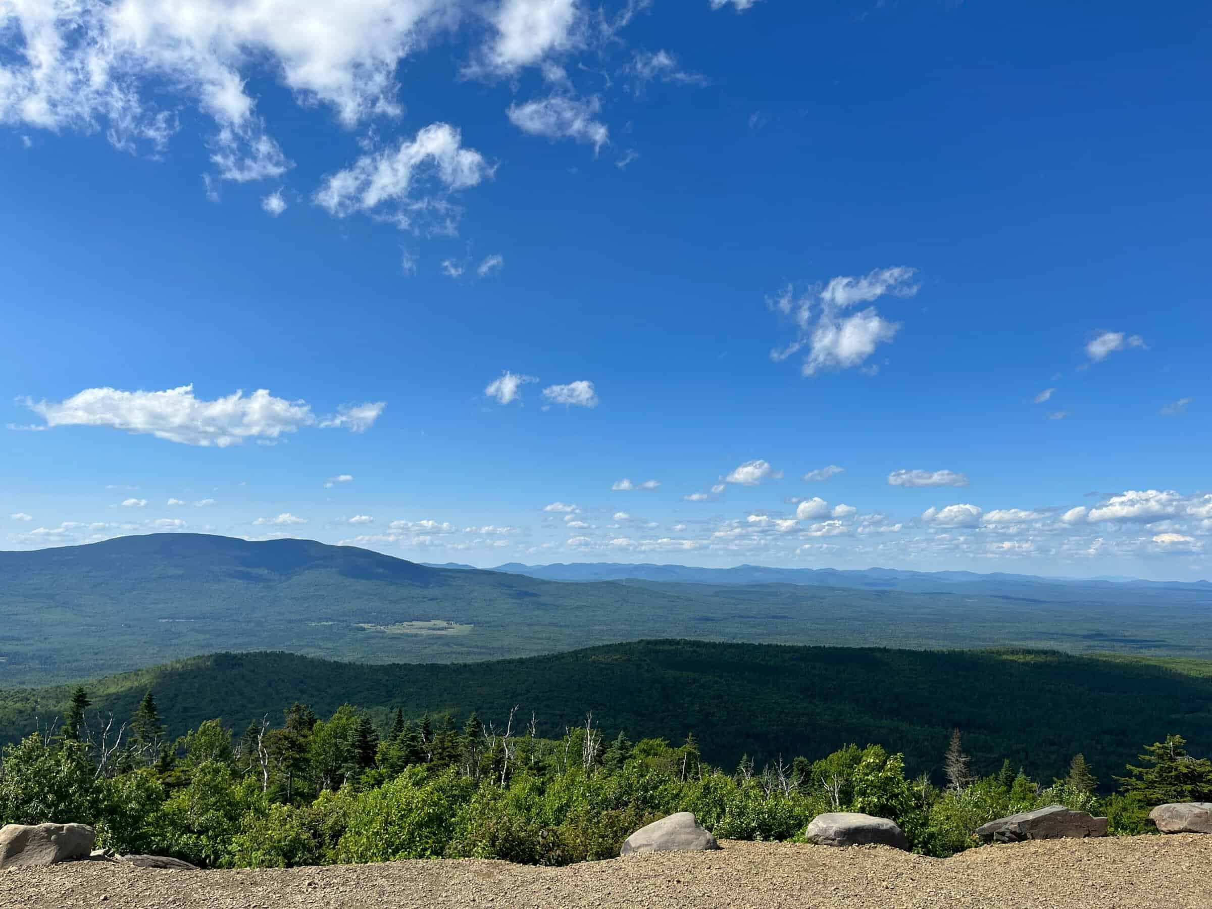Wide scenic view of rolling green hills and mountains under a blue sky