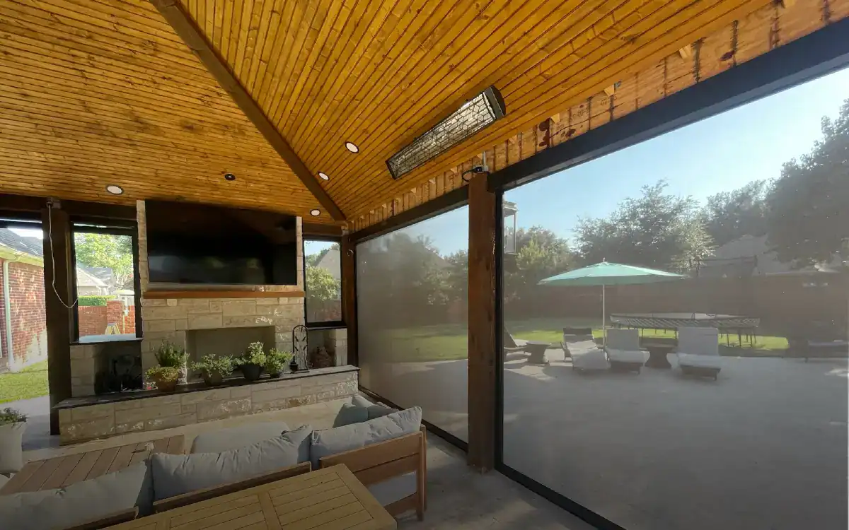 Indoor lounge area with large glass windows overlooking outdoor patio with umbrella and seating.
