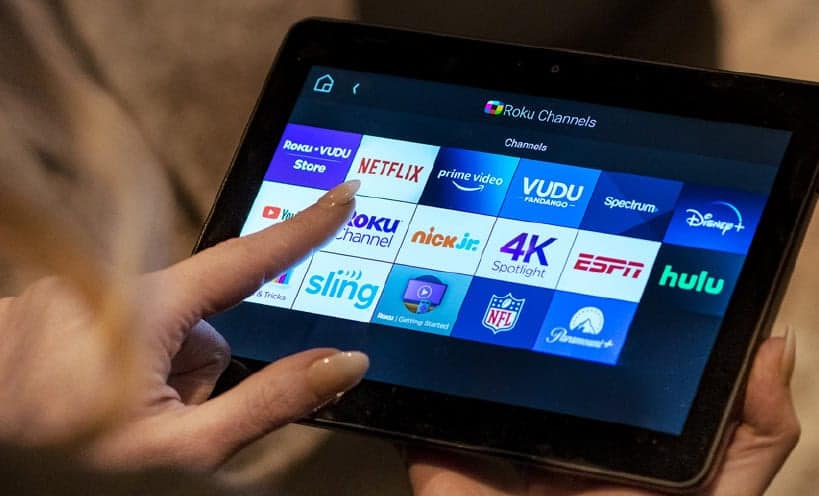 Person using a tablet to access streaming apps on a smart TV.